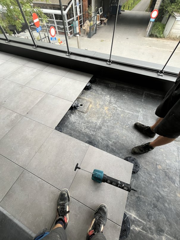 Betegeling van een balkon met glazen balustrade in uitvoering